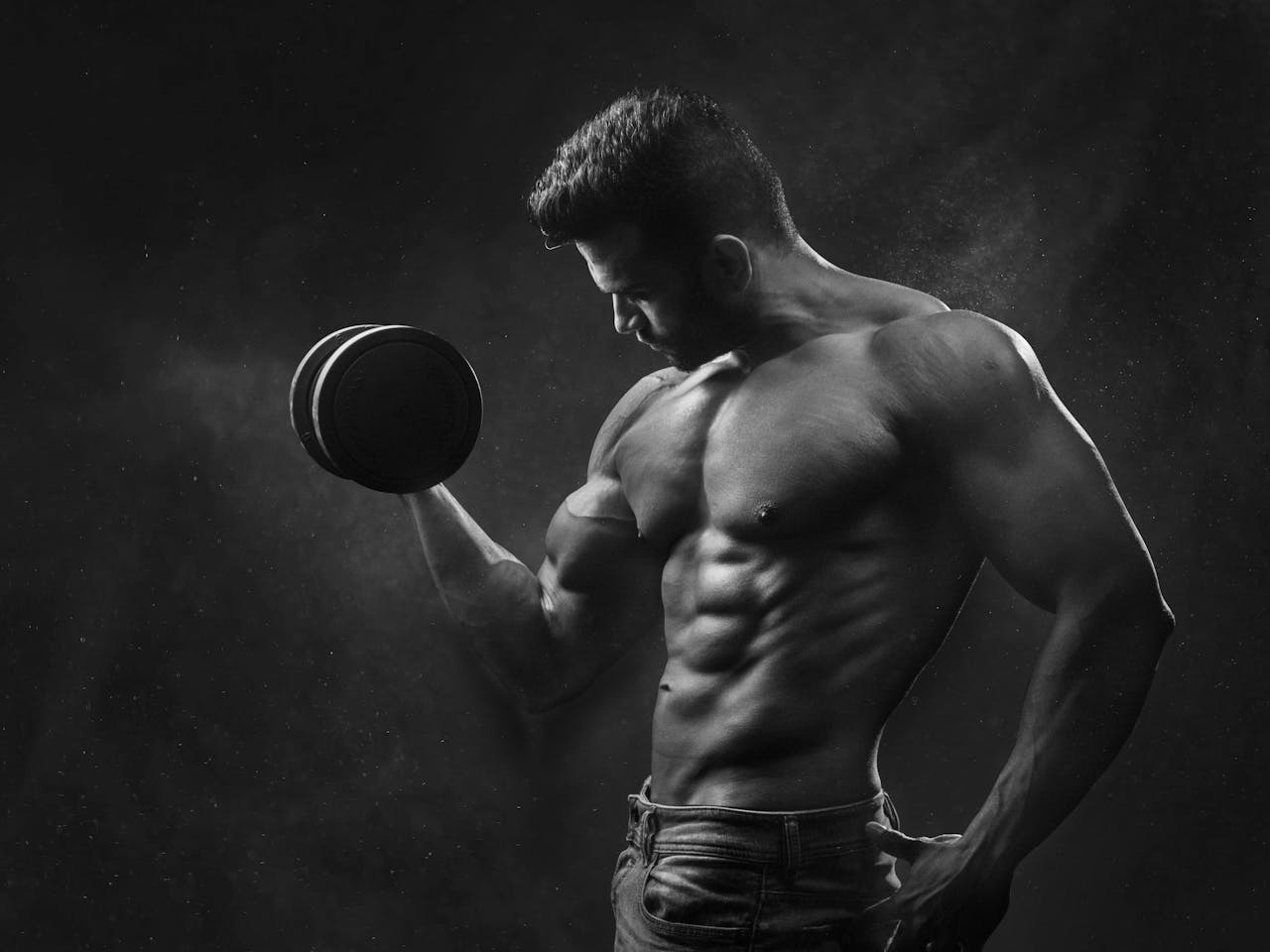 Home Powerful black and white portrait of a shirtless bodybuilder lifting dumbbells in the gym.